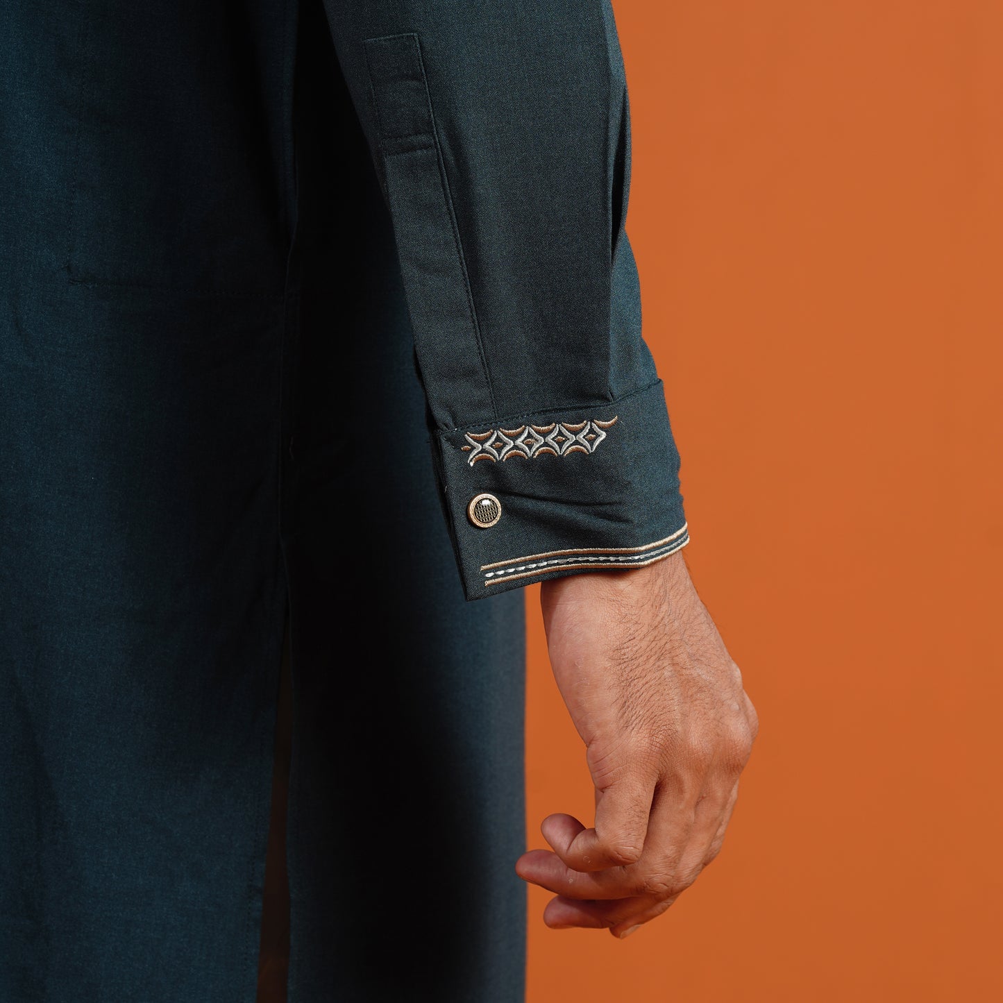 Close-up of a person wearing a dark blue garment with decorative cuffs against an orange background
