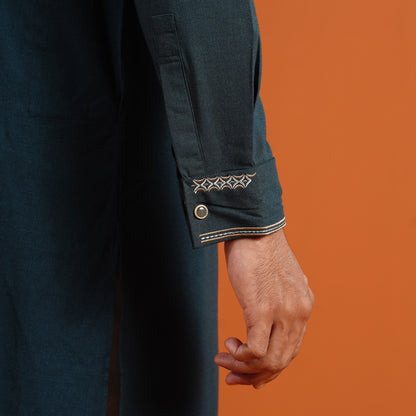 Close-up of a person wearing a dark blue garment with decorative cuffs against an orange background