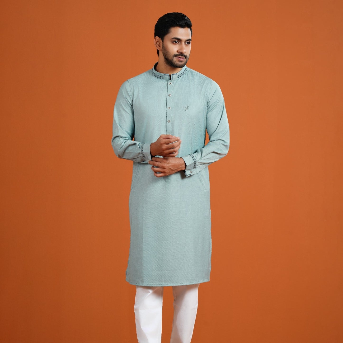 Man wearing a light blue kurta with white pants on an orange background