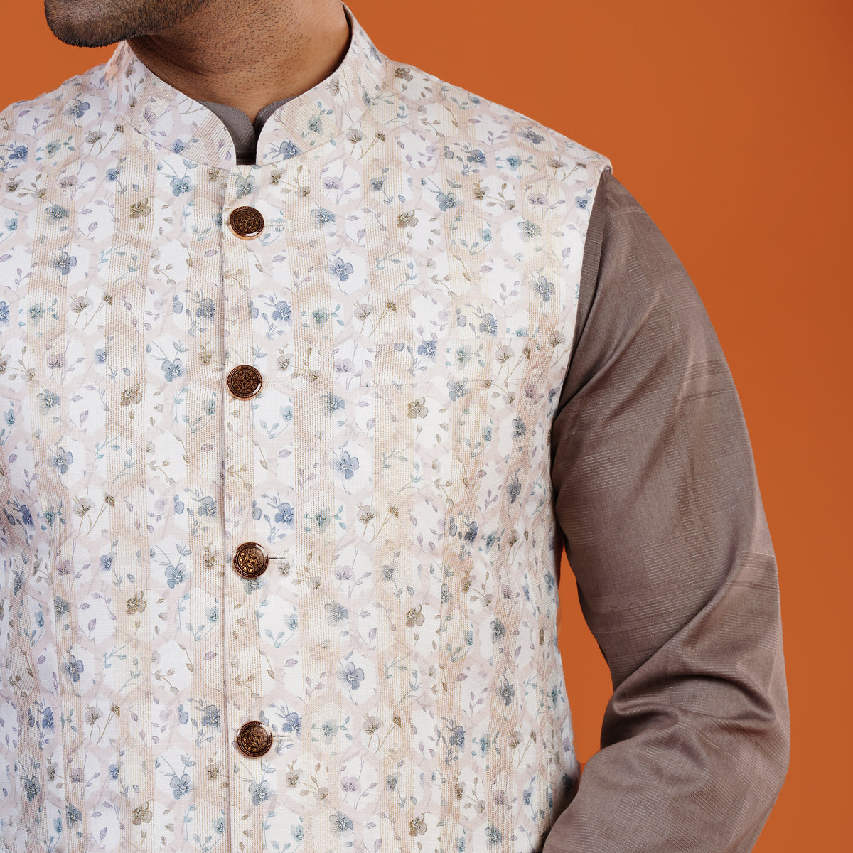 Person wearing a floral patterned vest over a brown shirt on an orange background