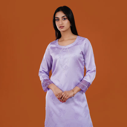 Woman wearing a light purple dress with intricate designs on an orange background