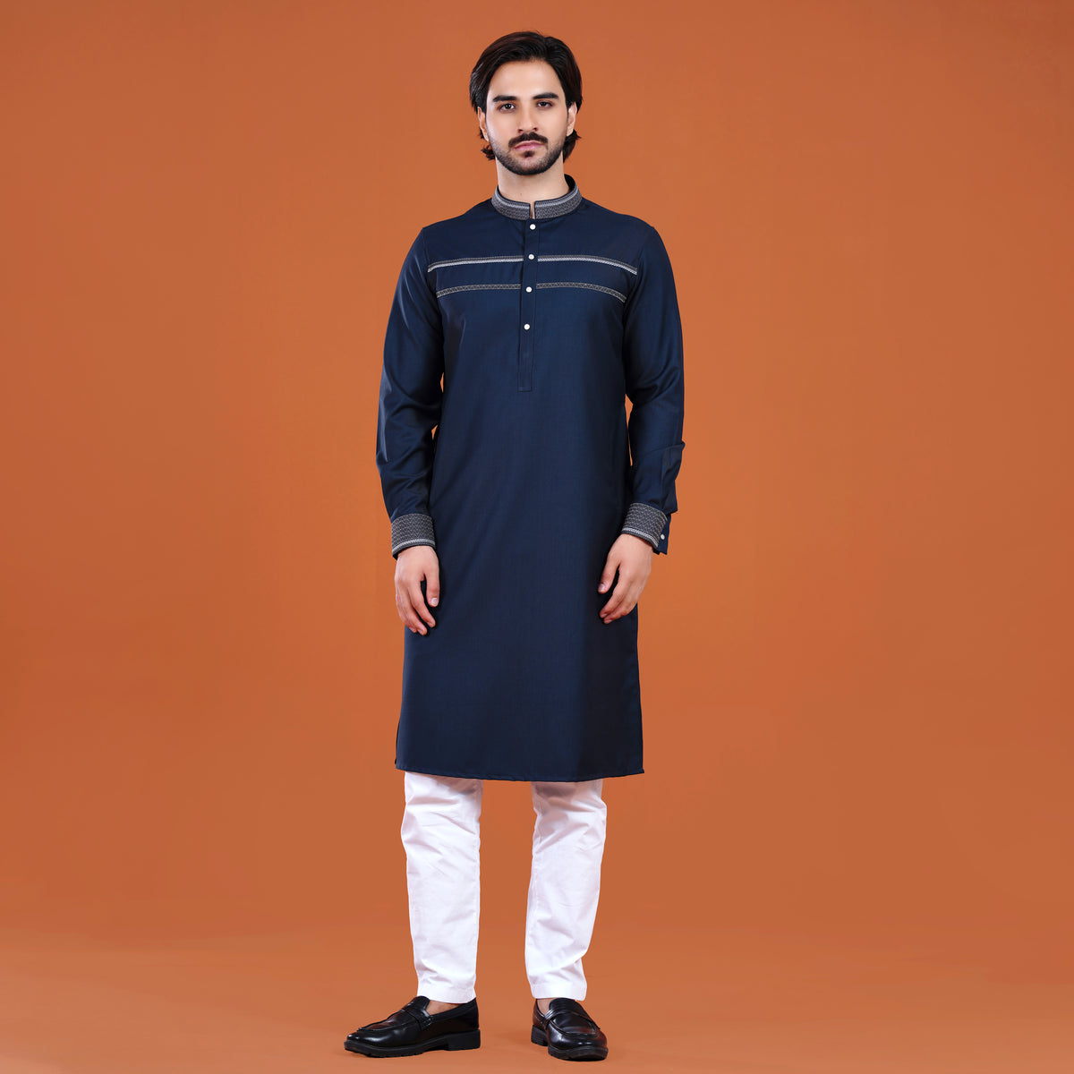 Man wearing a navy kurta with white pants on an orange background