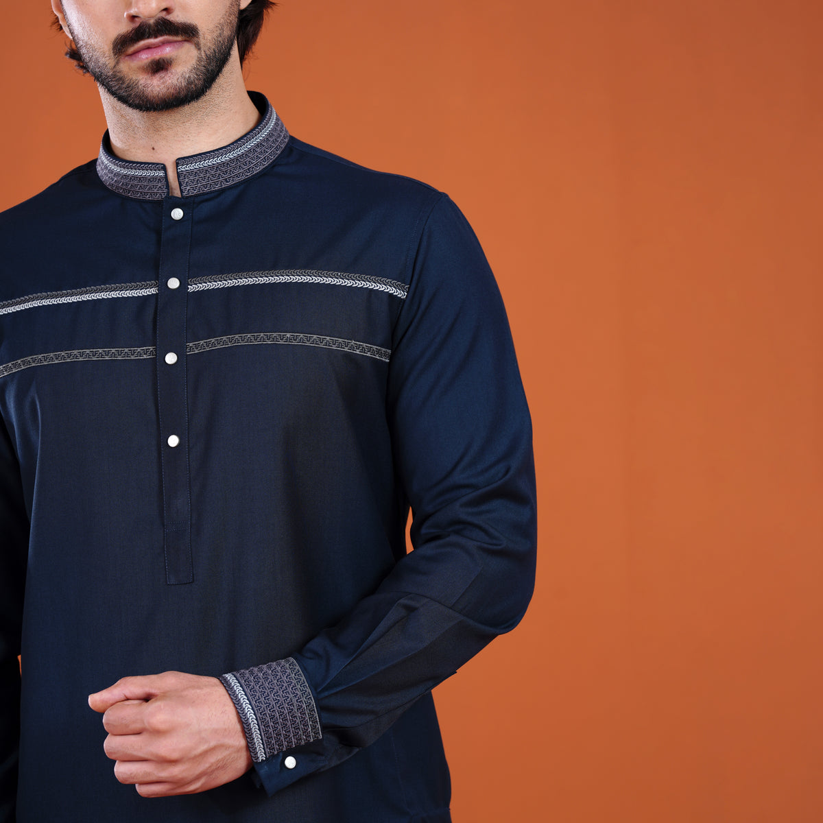 Man wearing a dark blue long-sleeve shirt with patterned collar and cuffs against an orange background