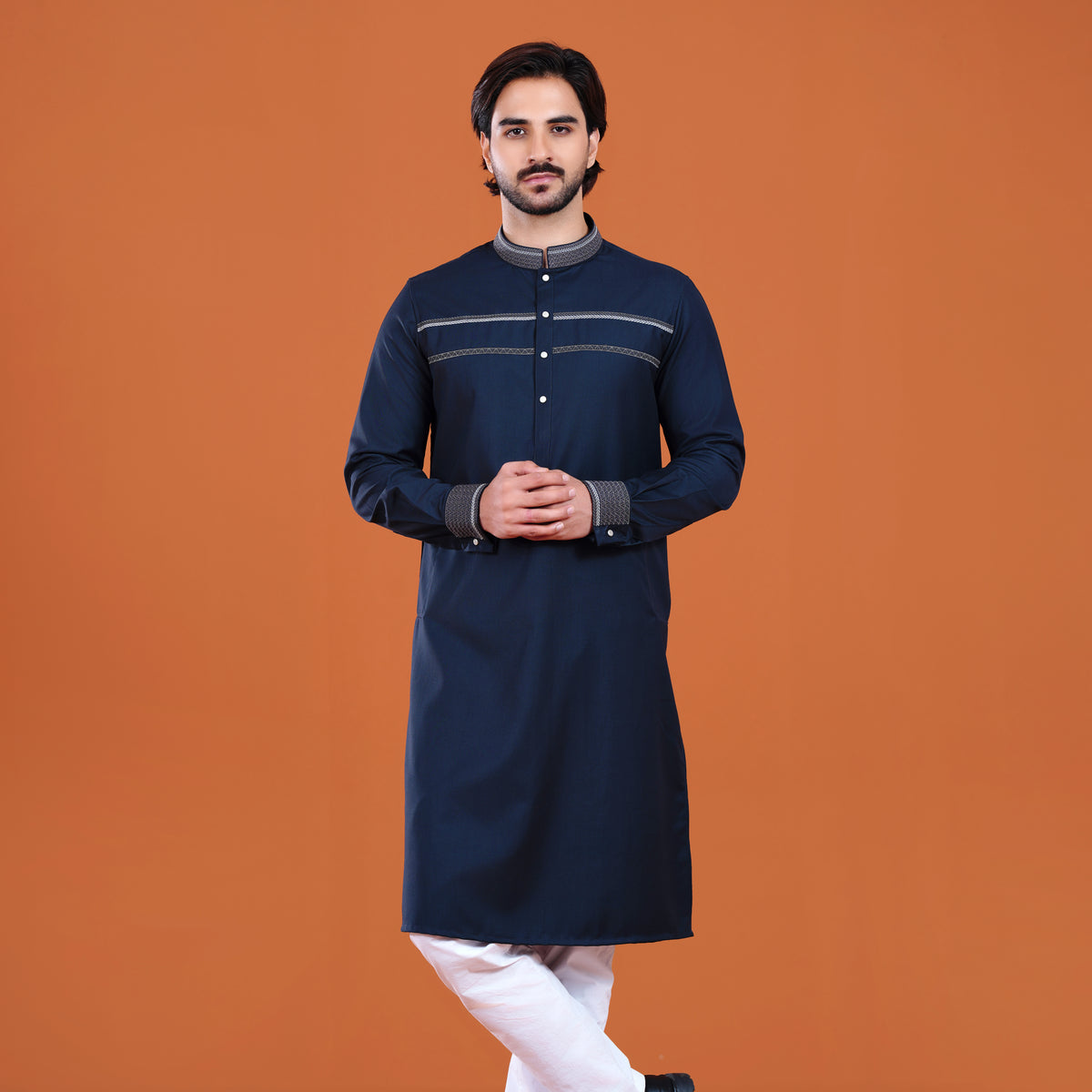 Man wearing a navy kurta with white pants against an orange background