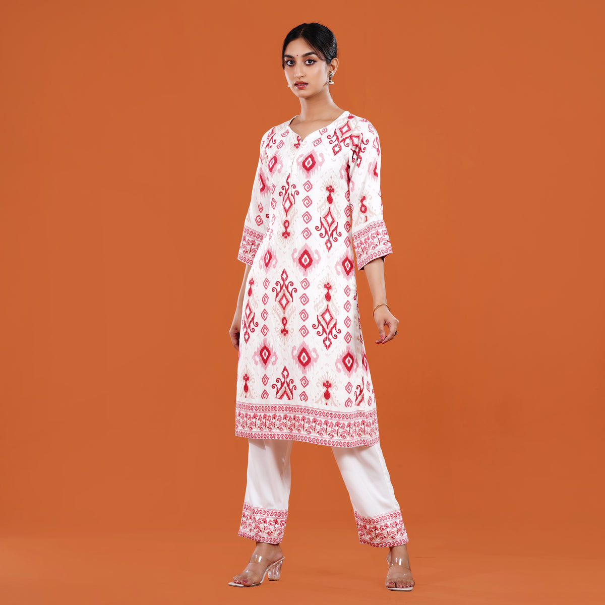 Woman wearing a white and red patterned kurta with white pants on an orange background