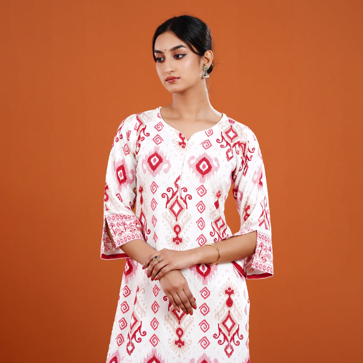 Woman wearing a white dress with red patterns against an orange background