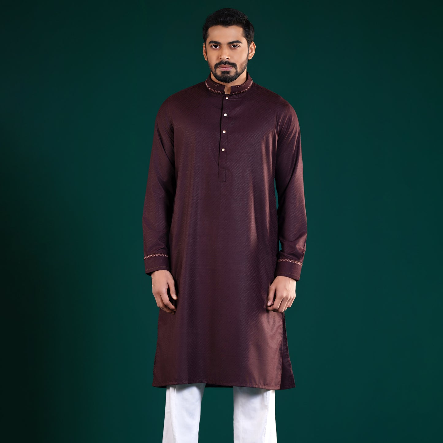 Man wearing a Yamaan Signature Panjabi maroon kurta with white pants on a dark green background