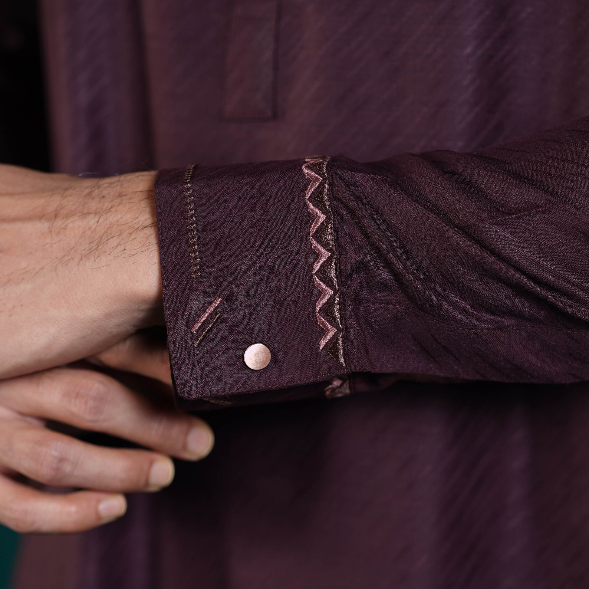 Close-up of a person adjusting the cuff of a Yamaan Signature Panjabi dark purple with intricate detailing.