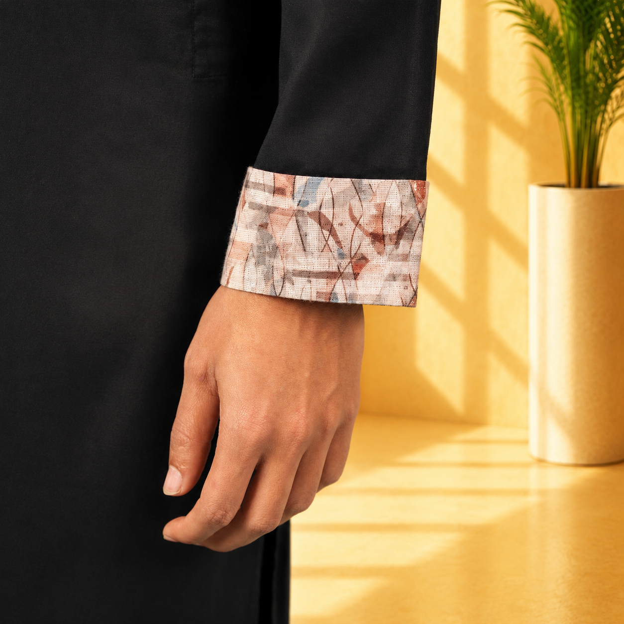 Person wearing a YAMAAN Royal Black Panjabi with a patterned cuff, standing against a yellow wall with a plant.