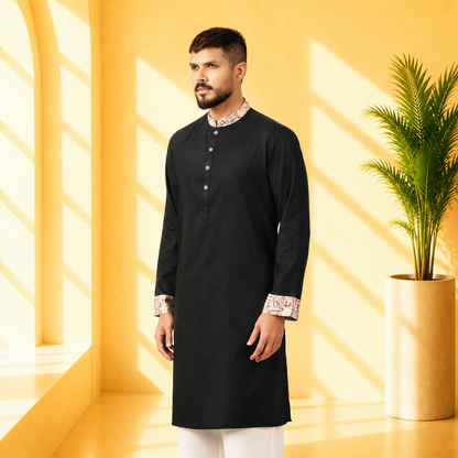 Man wearing a YAMAAN Royal Black Panjabi with white pants in a bright yellow room with a plant.