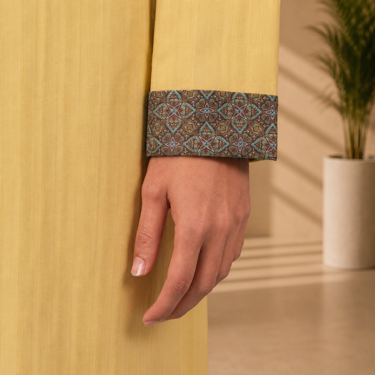 Close-up of a hand wearing a YAMAAN Royal Mustard Panjabi with a plant in the background.
