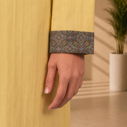 Close-up of a hand wearing a YAMAAN Royal Mustard Panjabi with a plant in the background.