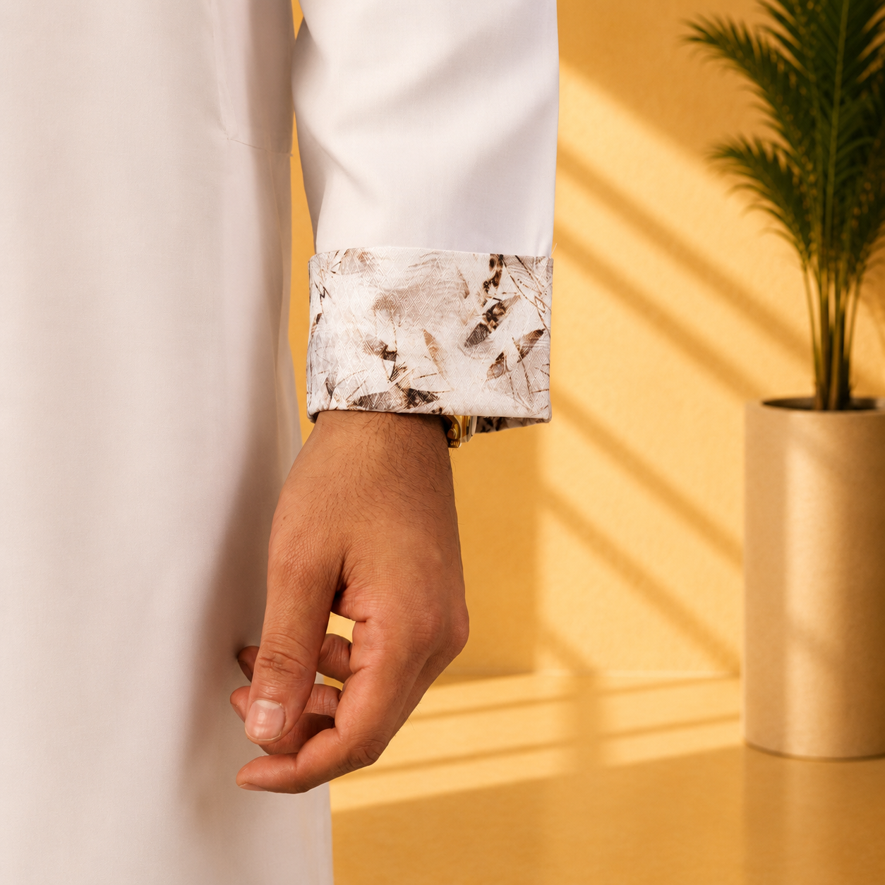 Close-up of a hand wearing a yamaan royal panjabi with a yellow wall and plant in the background
