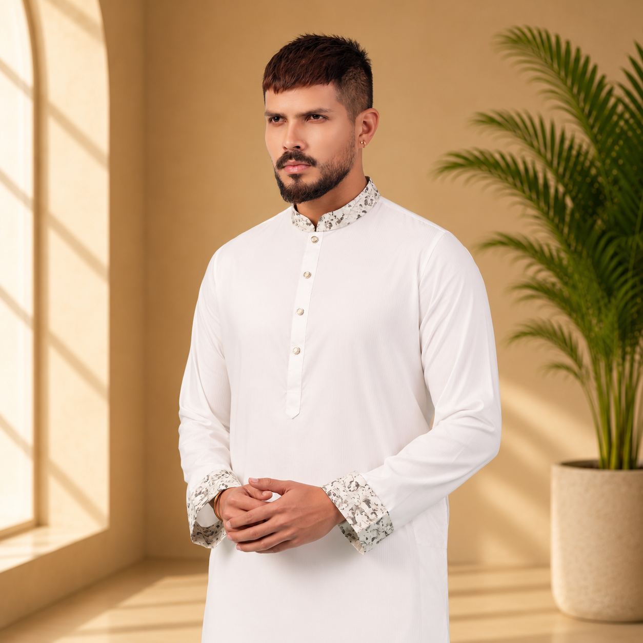 Man wearing a yamaan royal panjabi with cuffs details in a room with a plant and window.