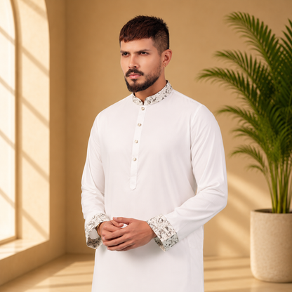 Man wearing a yamaan royal panjabi with cuffs details in a room with a plant and window.