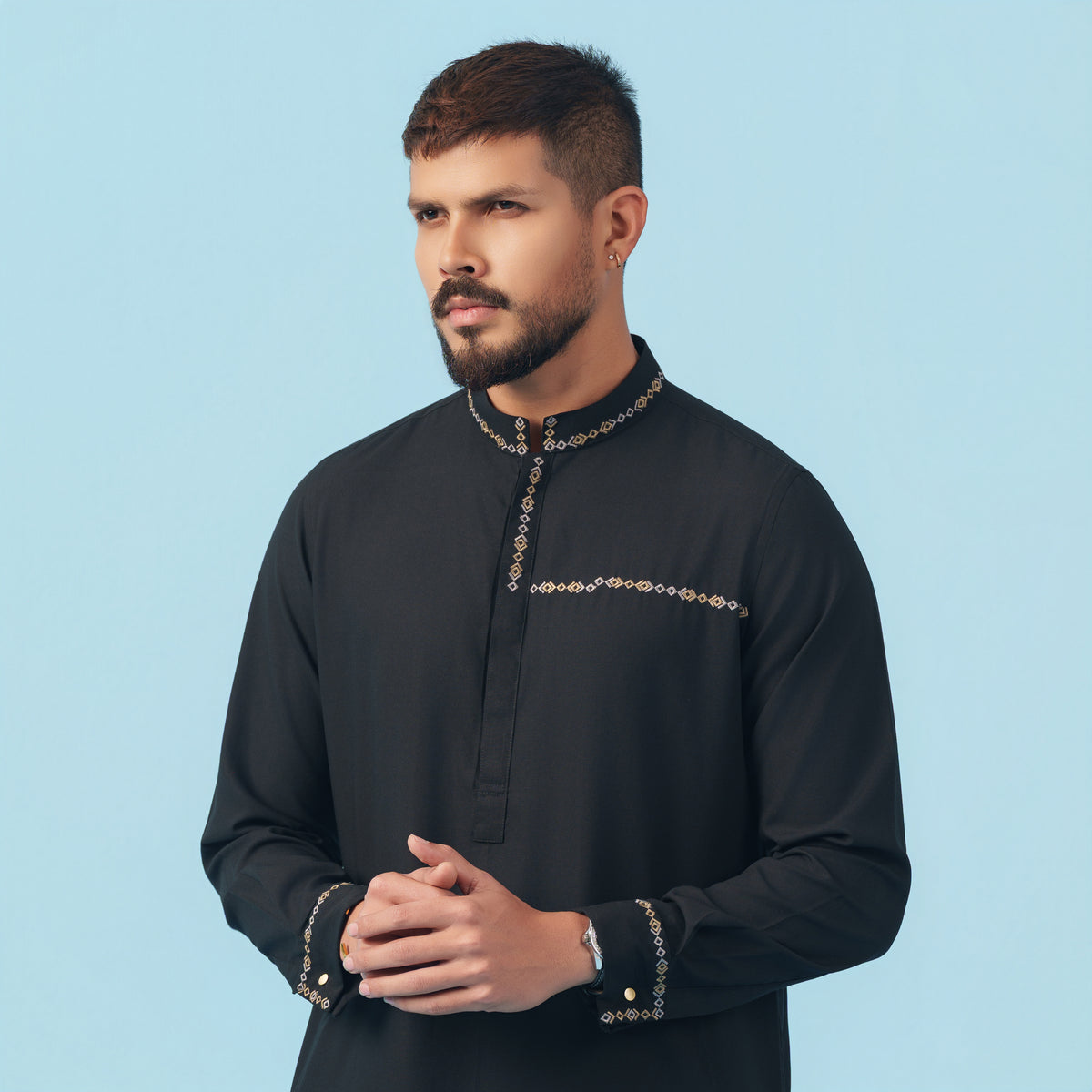 Man wearing a black yamaan panjabi outfit with intricate designs on a light blue background