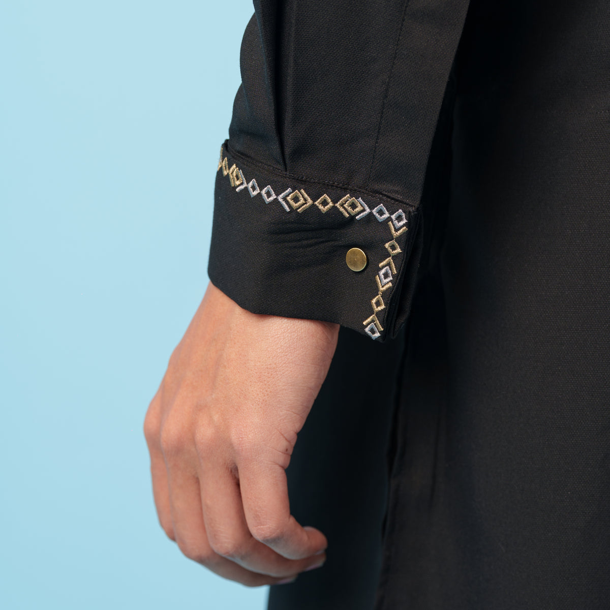 Close-up of a yamaan panjabi with decorative cuffs on a light blue background