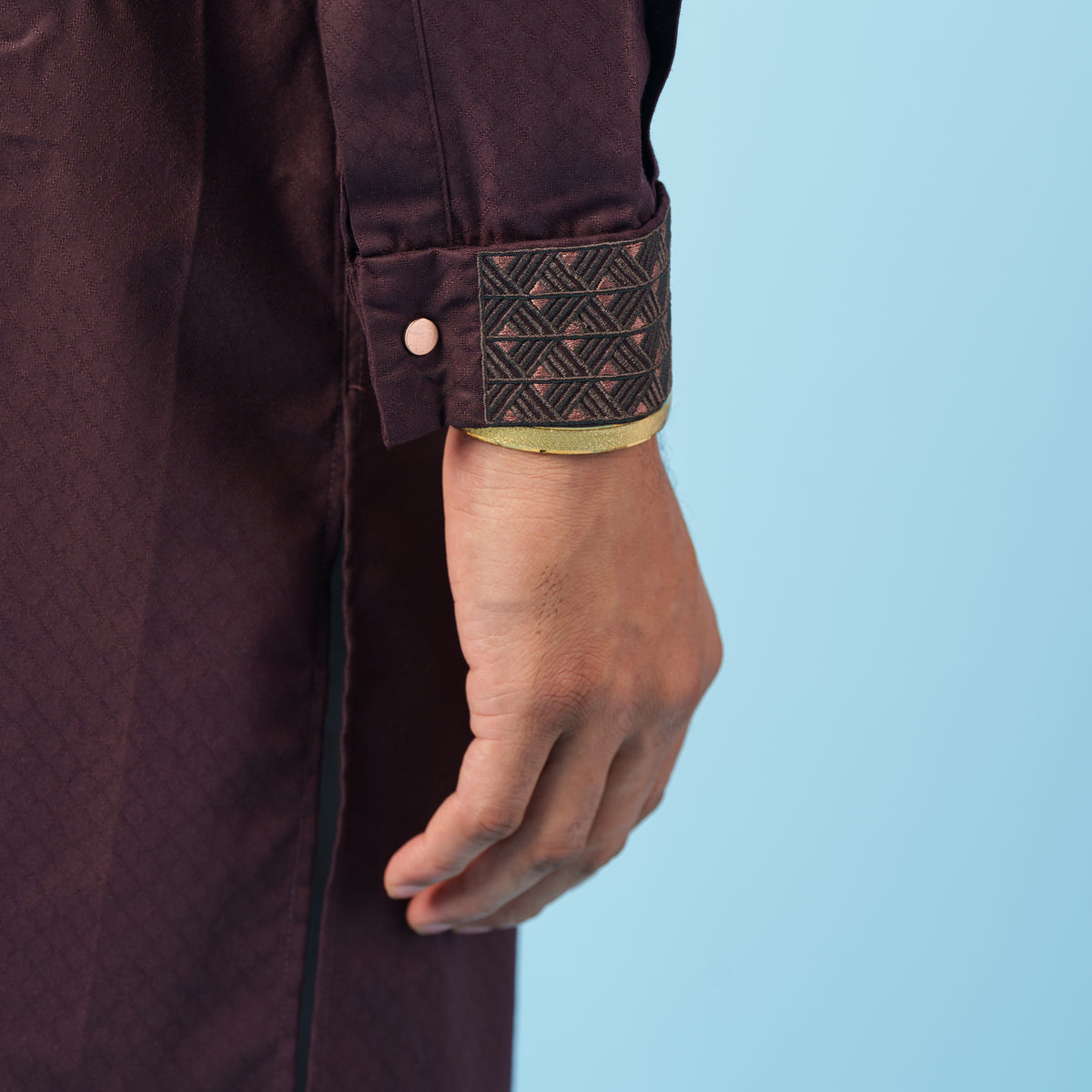 Close-up of a person wearing a yamaan panjabi with a textured cuff against a light blue background