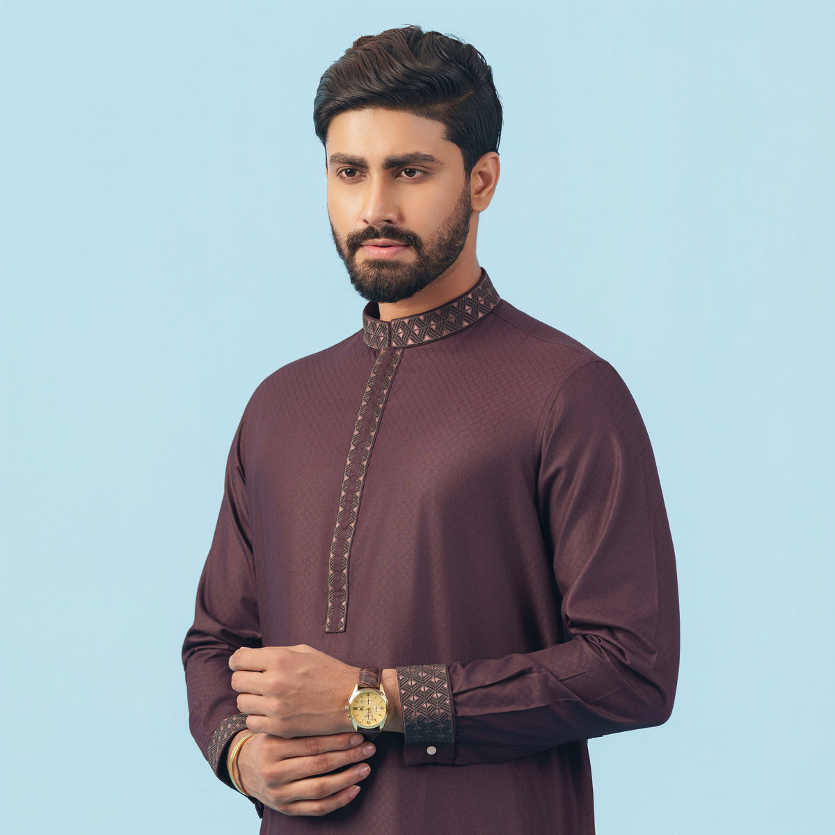 Man wearing a yamaan signature panjabi a traditional outfit with intricate details on a light blue background