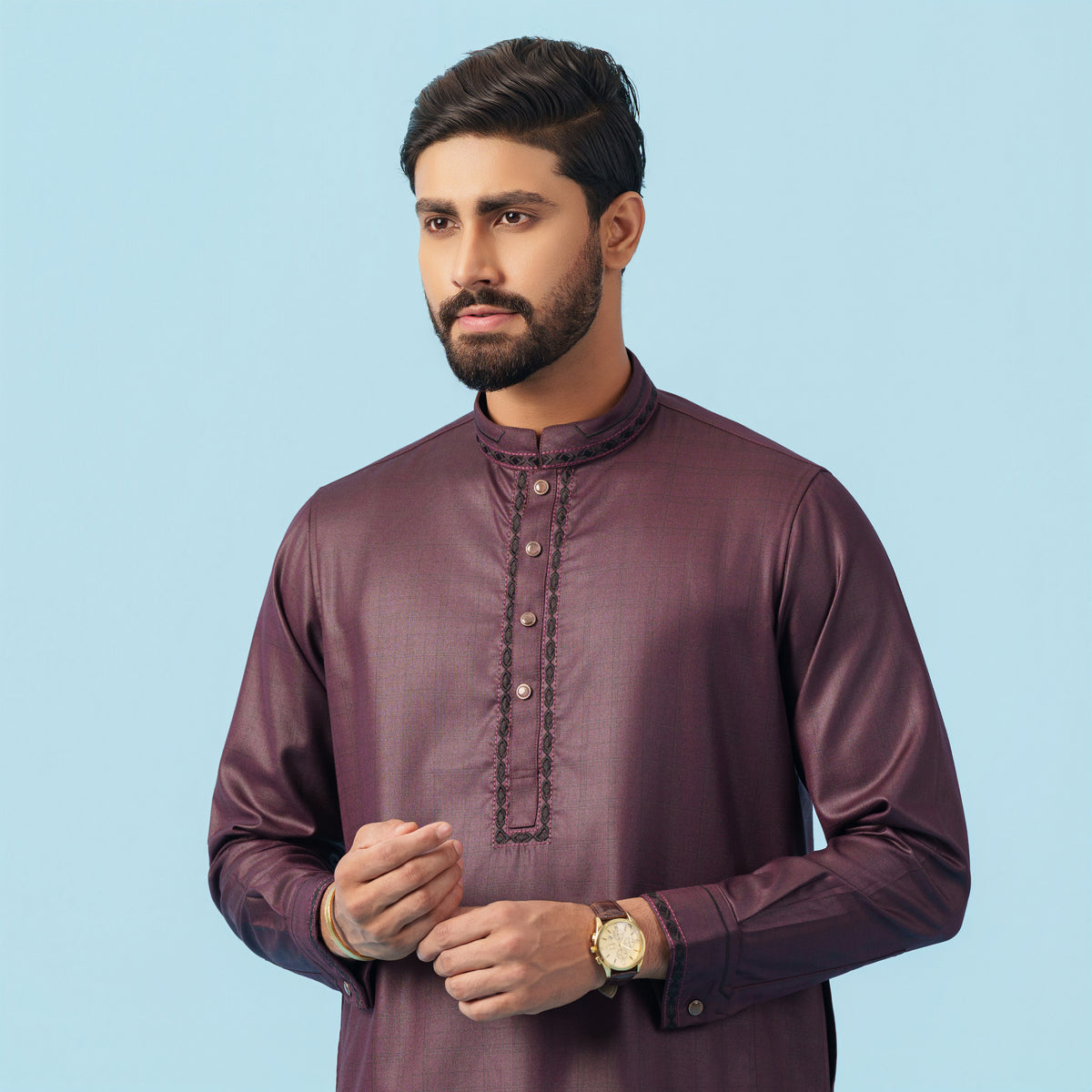 Man wearing a maroon traditional kurta against a light blue background