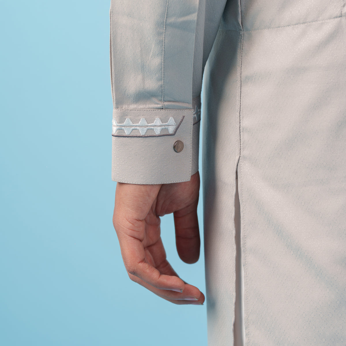 Close-up of a yamaan signature panjabi with a hand wearing a ring on a blue background