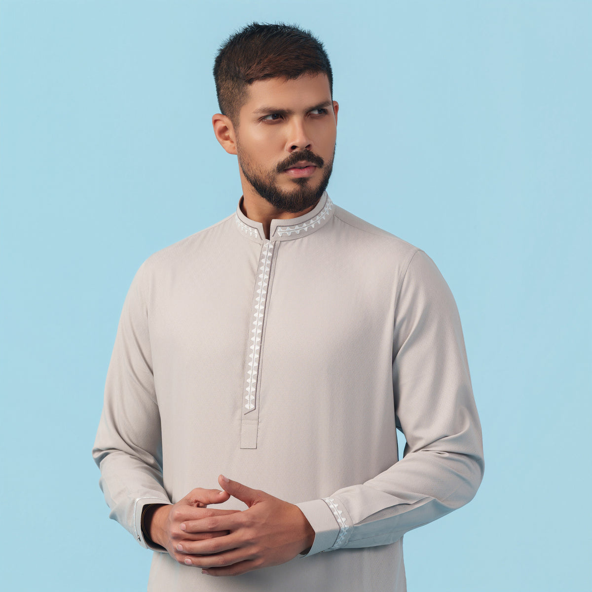 Man wearing a light gray yamaan panjabi traditional outfit with white embroidery on a blue background