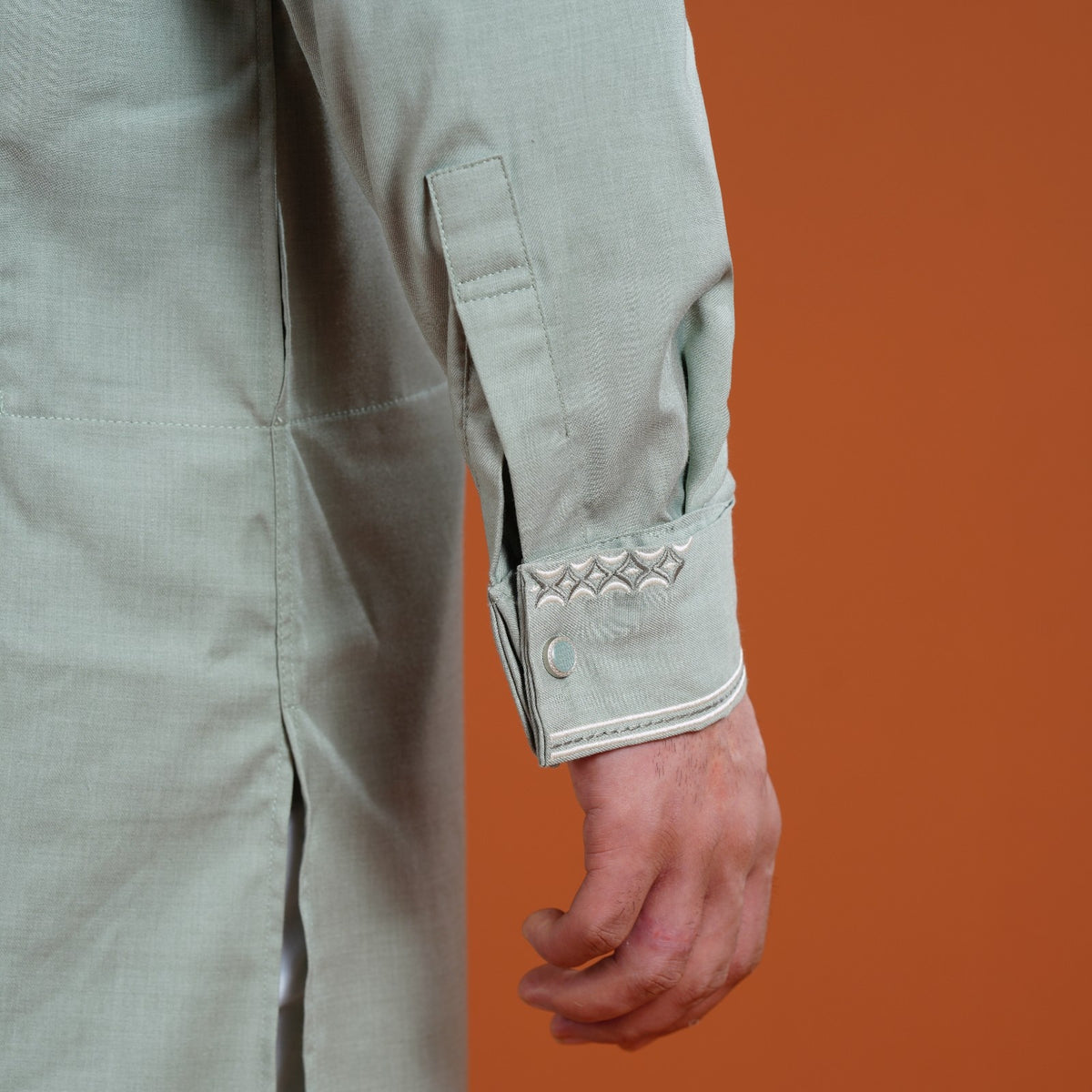 Close-up of a yamaan panjabi with decorative cuffs on an orange background