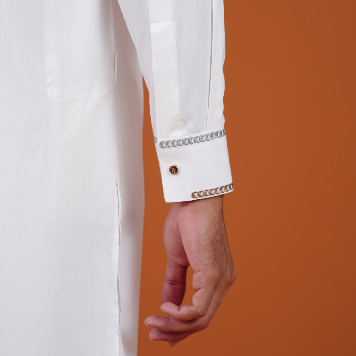 Close-up of a yamaan white signature panjabi sleeve with decorative trim against an orange background