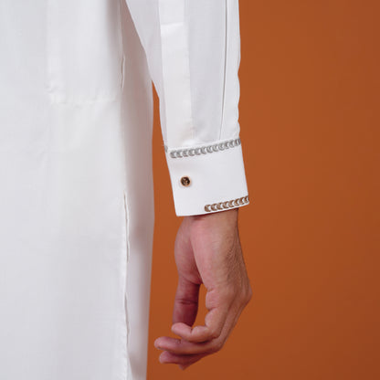Close-up of a yamaan white signature panjabi sleeve with decorative trim against an orange background