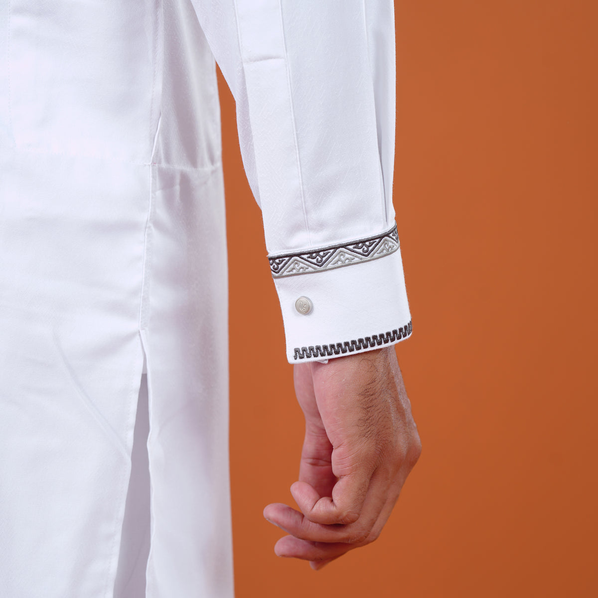 Close-up of a white yamaan panjabi with decorative cuffs against an orange background