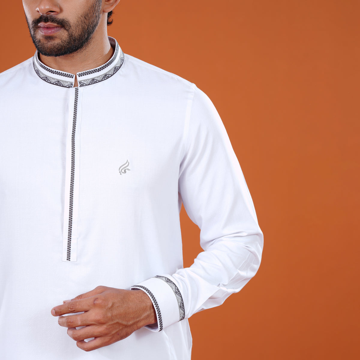 Man wearing a white traditional yamaan panjabi with intricate detailing on an orange background