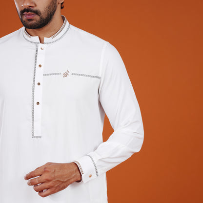 Man wearing a white yamaan signature panjabi traditional outfit with intricate details on an orange background